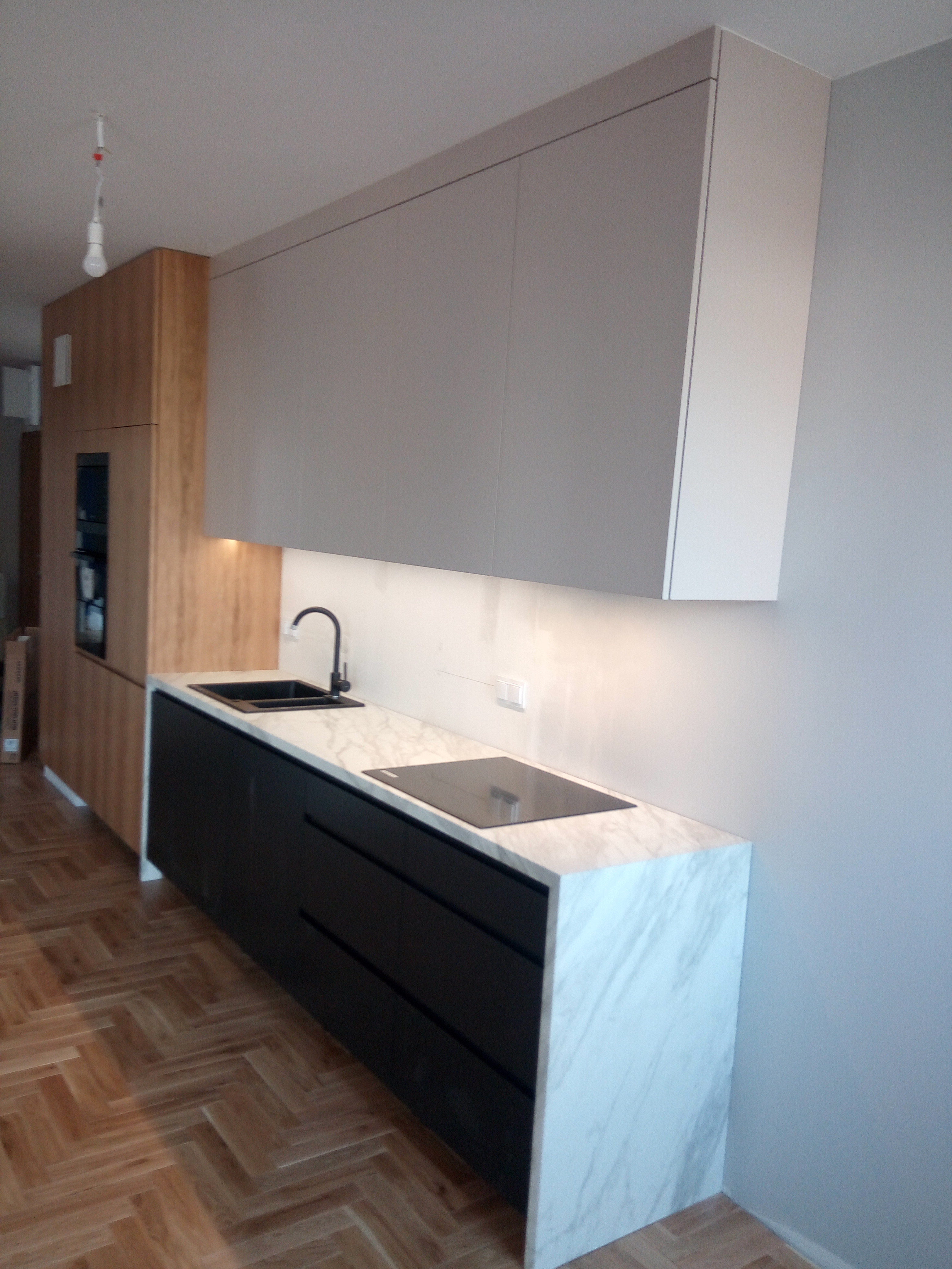 Kuchnia z czarnymi dolnymi szafkami i blatami w stylu marmuru