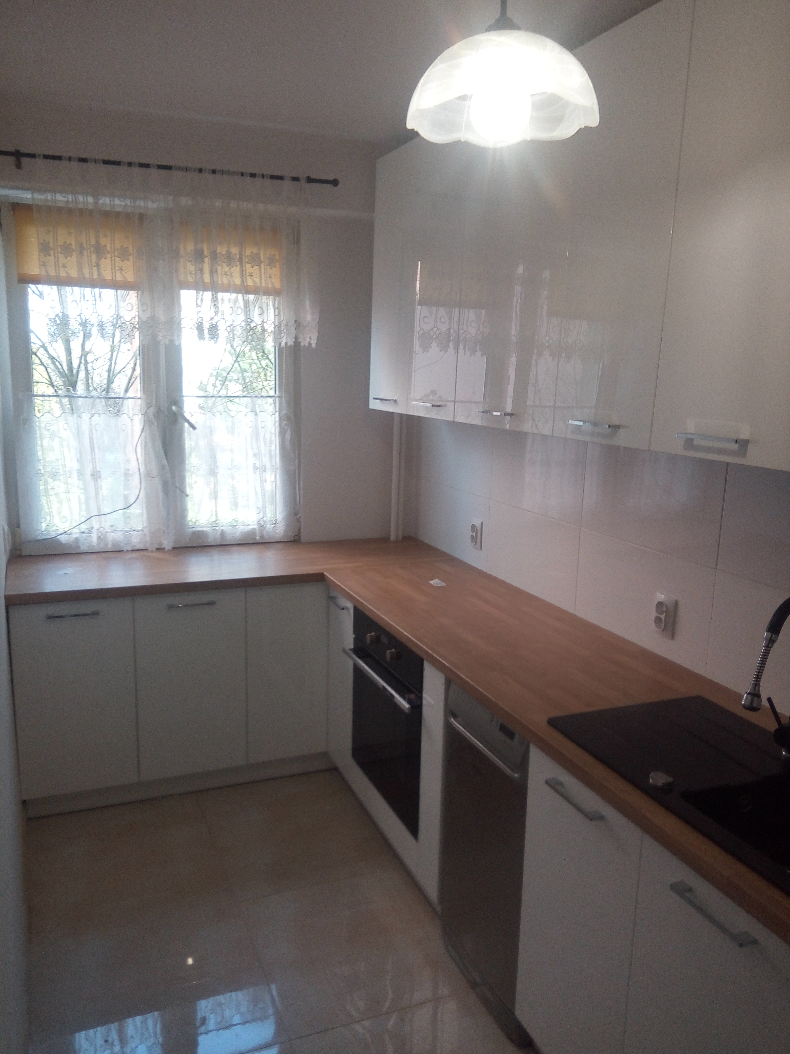 Wąska kuchnia z białymi frontami i drewnianym blatem