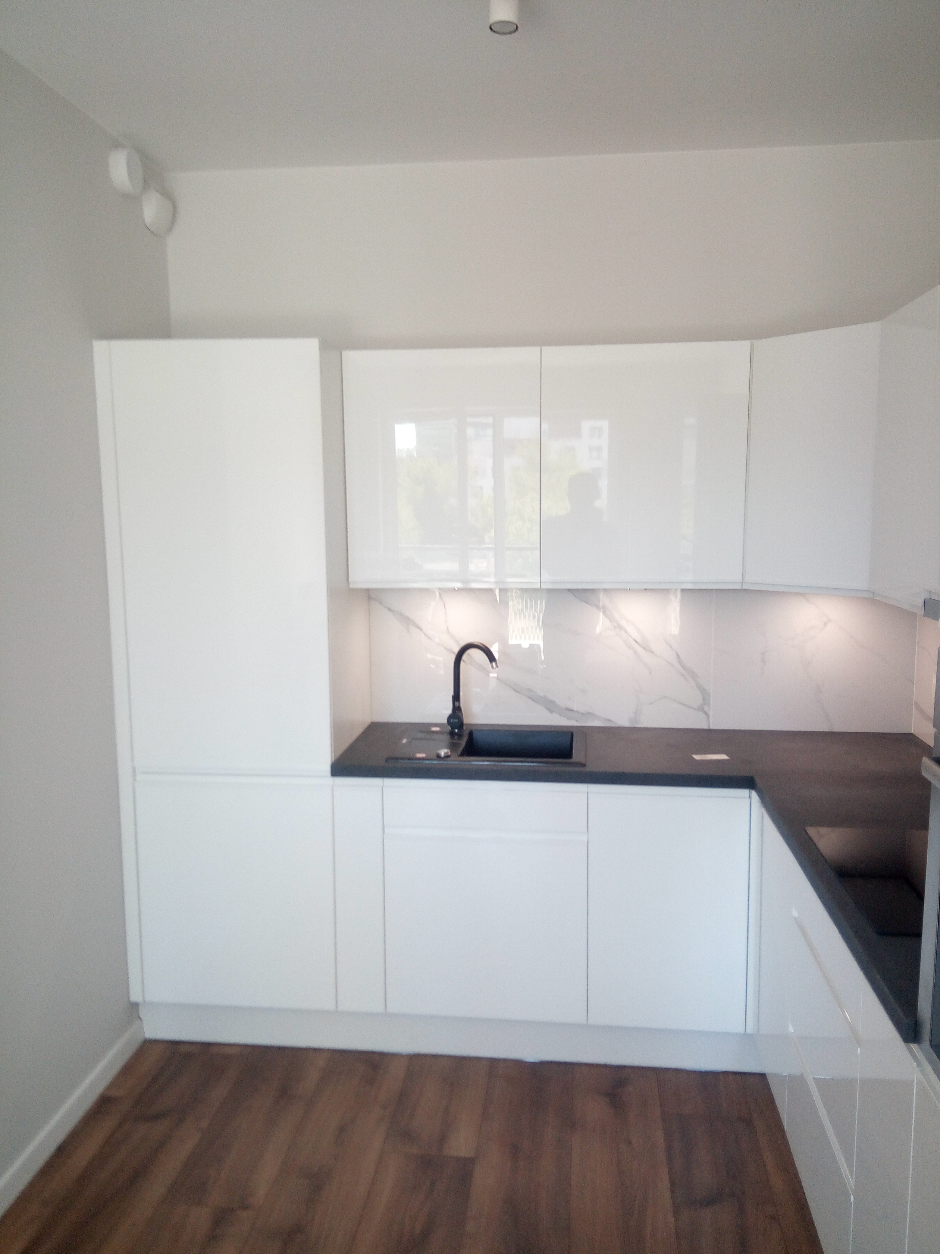 Biała kuchnia z ciemnym blatem i marmurową ścianą