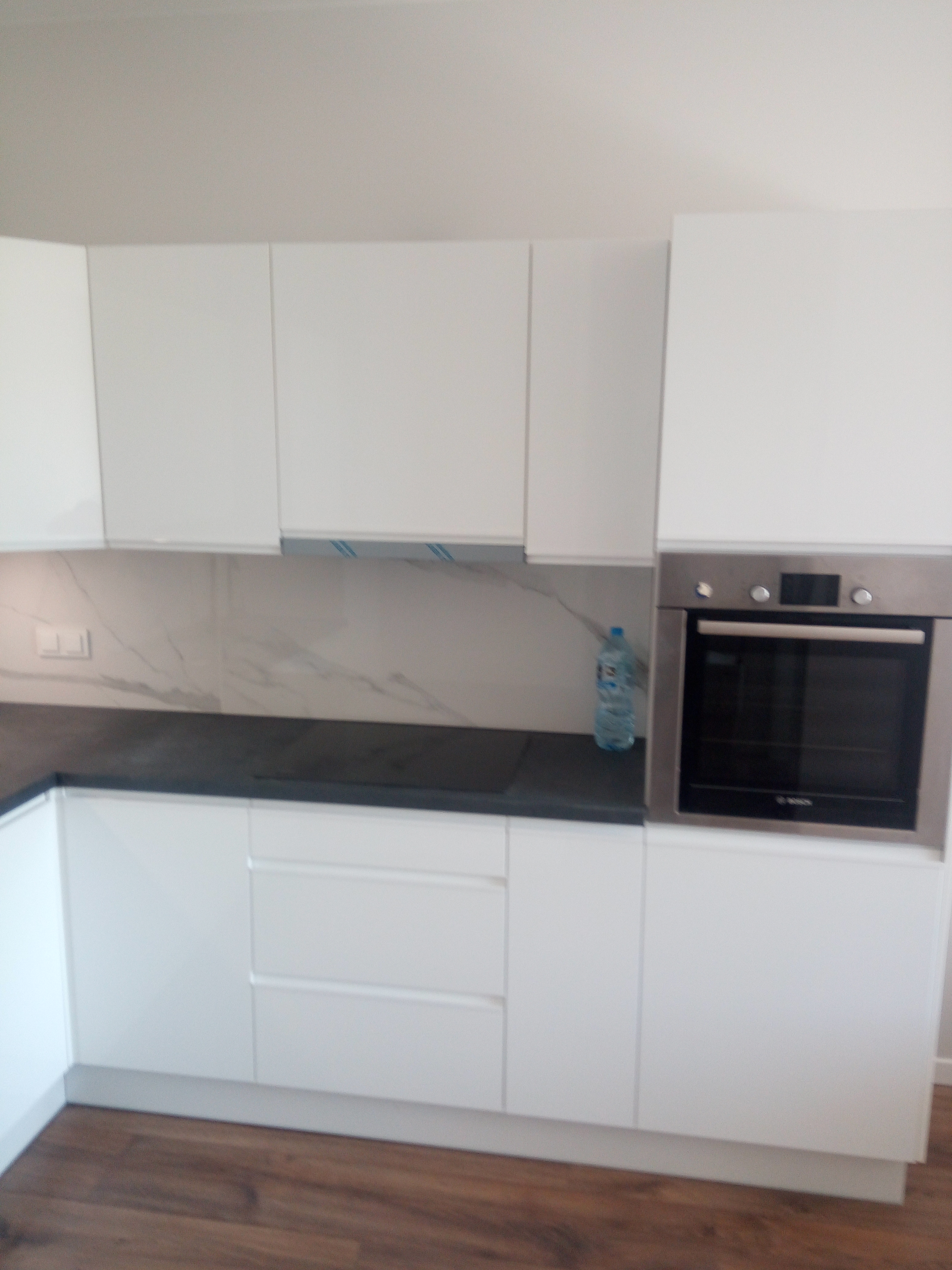 Kuchnia w bieli z ciemnym blatem i drewnianą podłogą